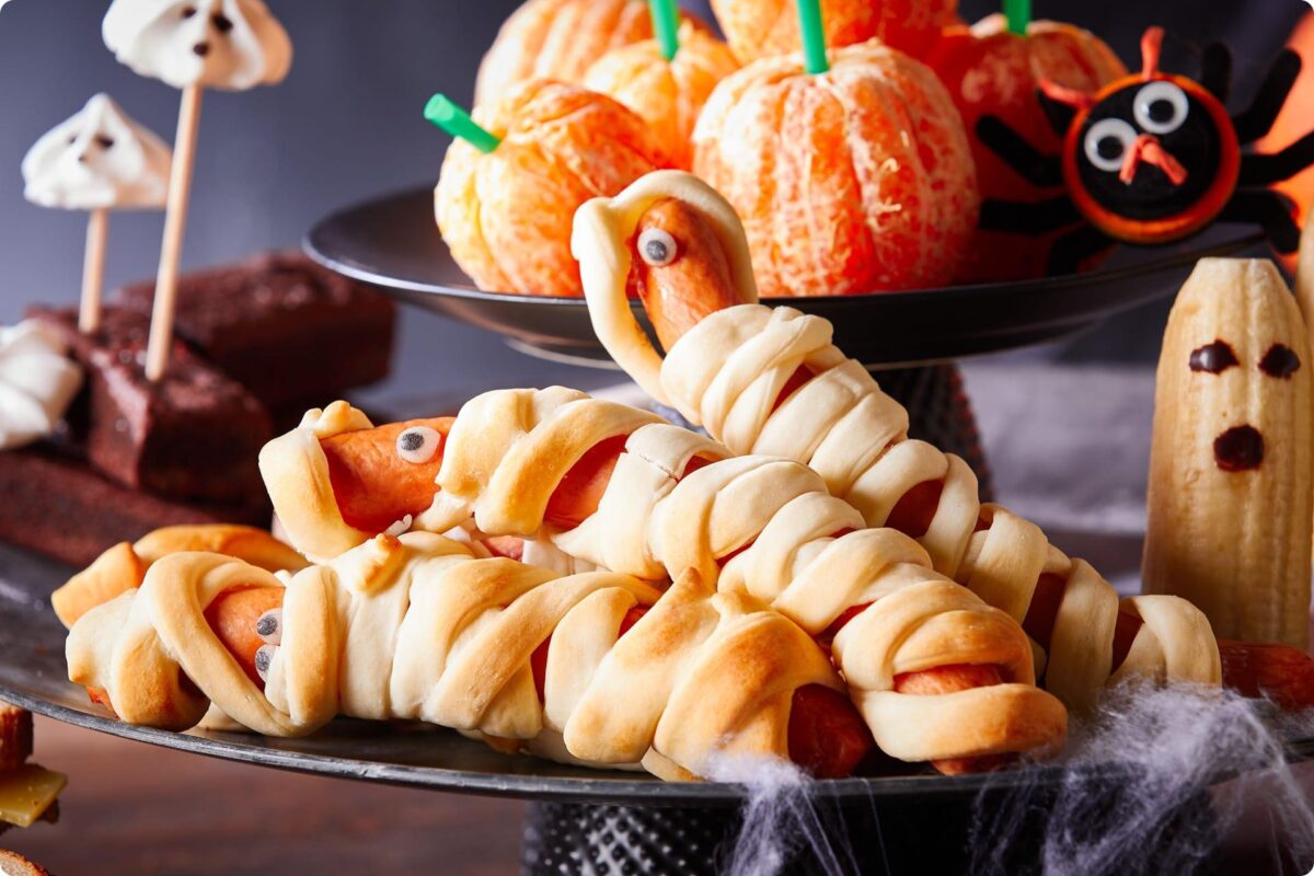 Halloweenské občerstvení na párty – párky v listovém těstě jako mumie, mandarinkové dýně a sladkosti ve tvaru duchů.